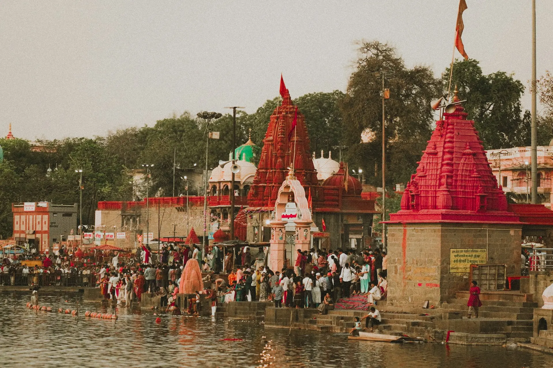 Crowd gathers by river near colorful temples